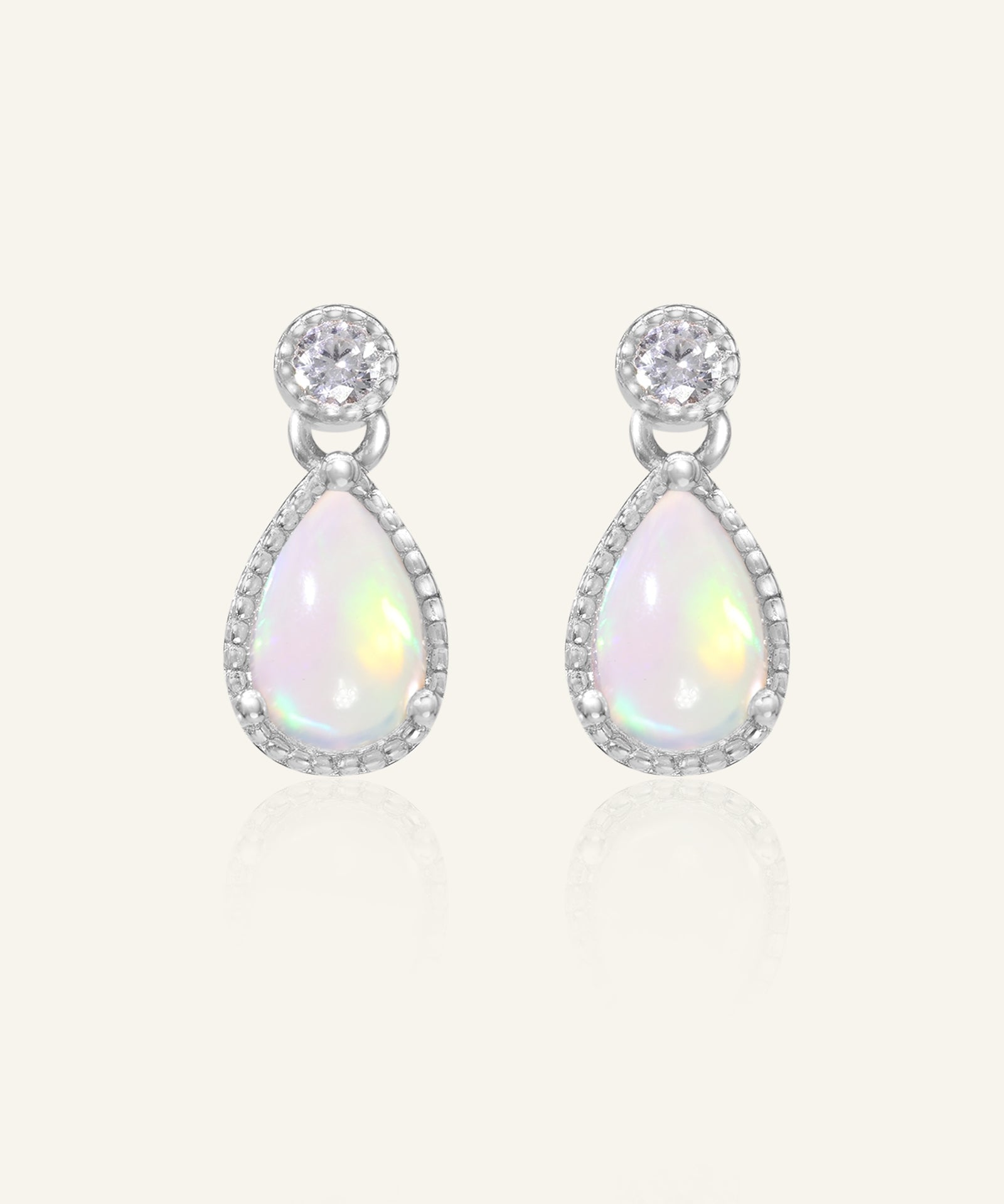Suri Opal Teardrop Studs in silver, resting on a warm linen background