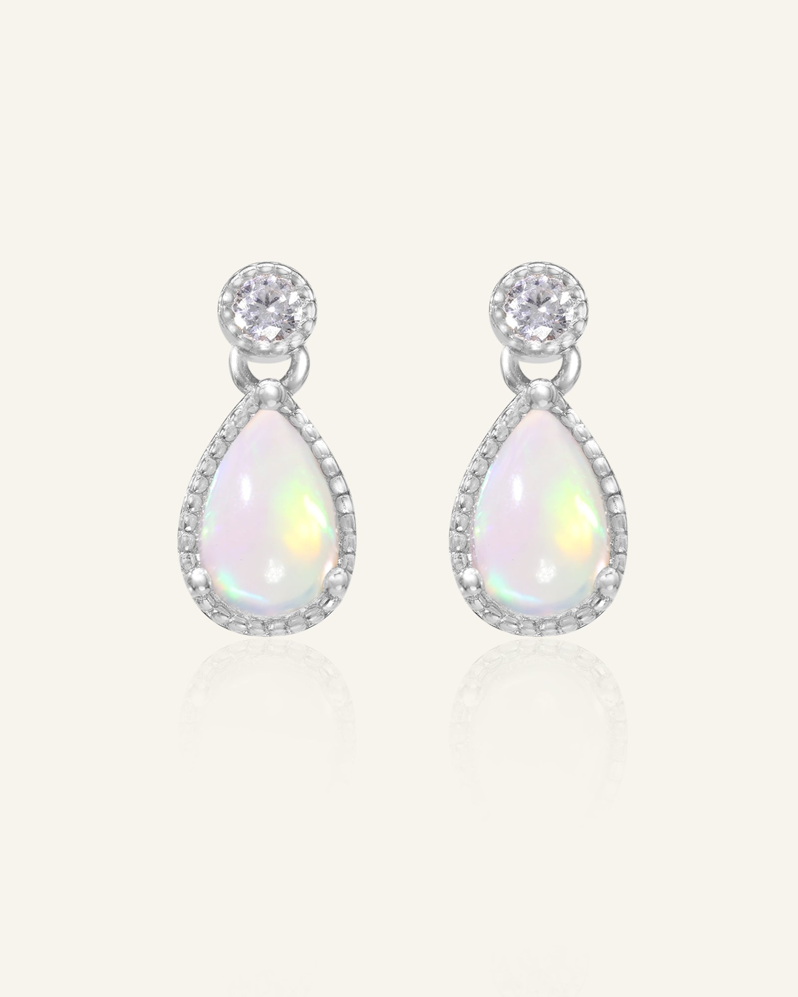 Suri Opal Teardrop Studs in silver, resting on a warm linen background