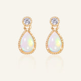 Suri Opal Teardrop Studs in yellow gold, resting on a warm linen background