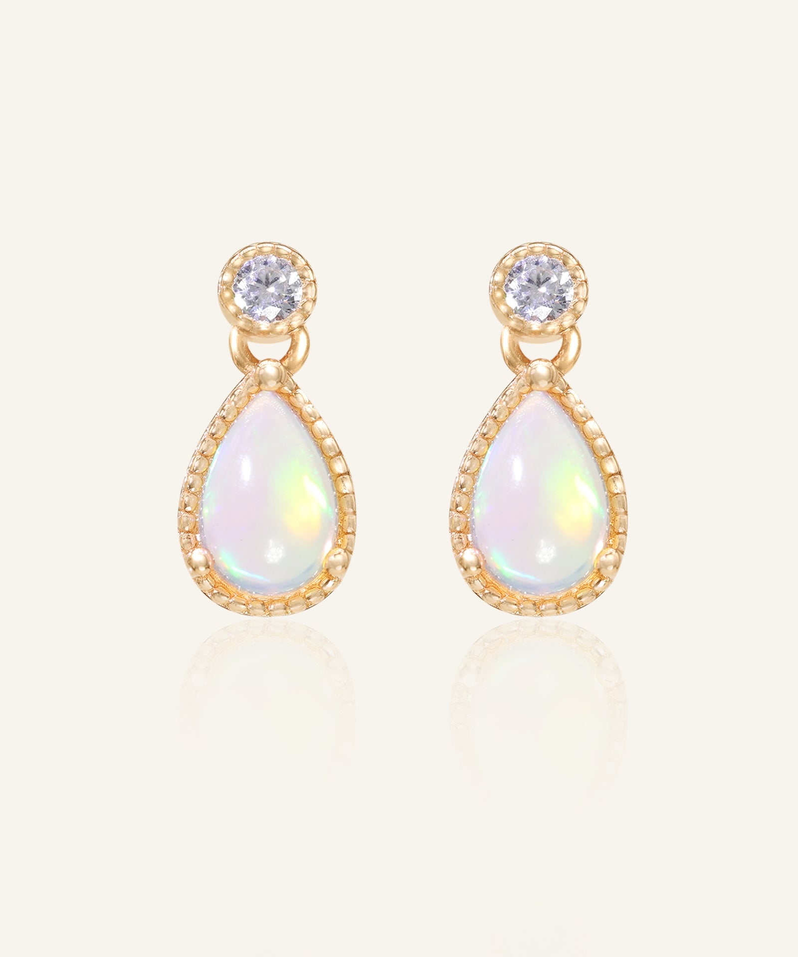 Suri Opal Teardrop Studs in yellow gold, resting on a warm linen background
