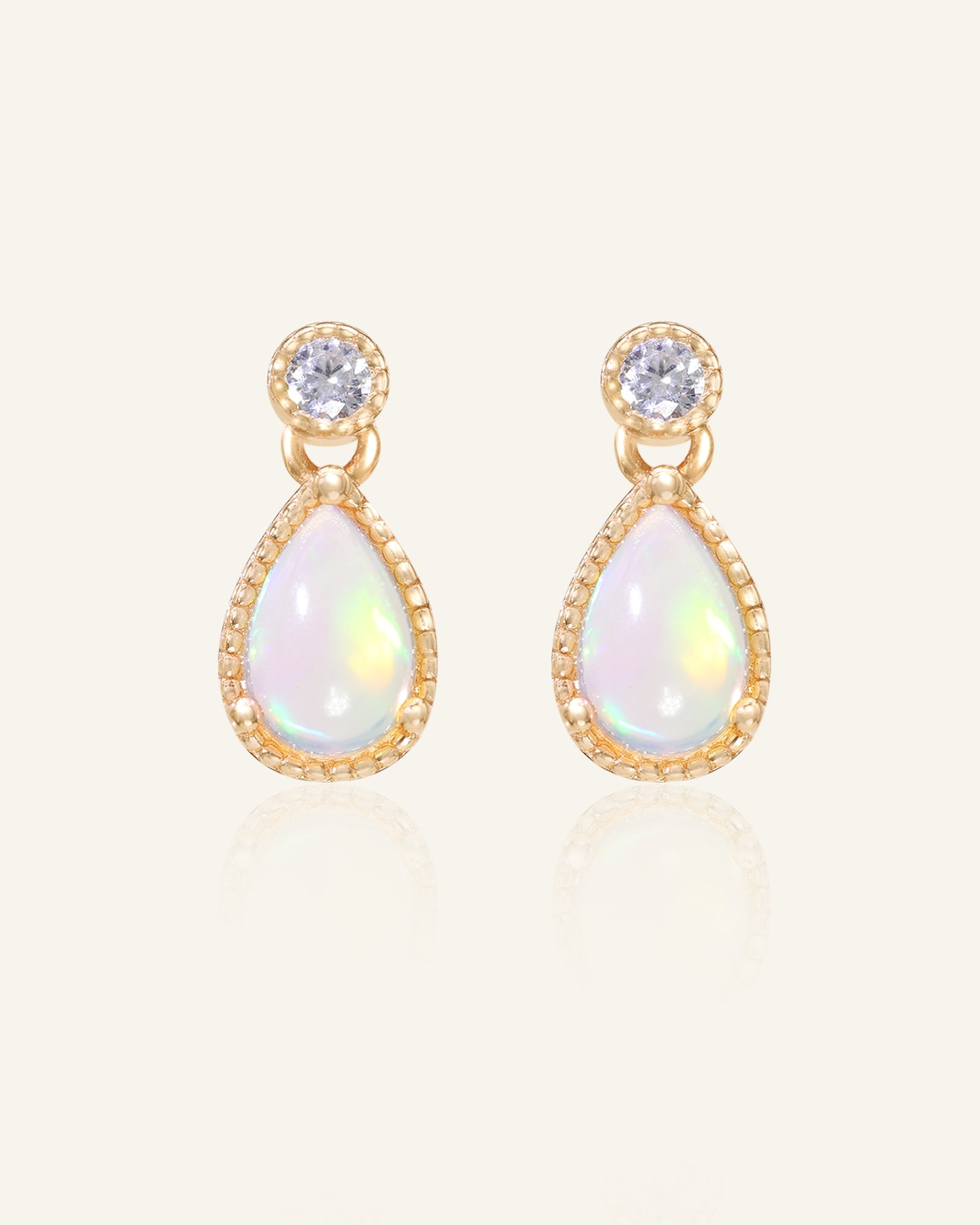 Suri Opal Teardrop Studs in yellow gold, resting on a warm linen background