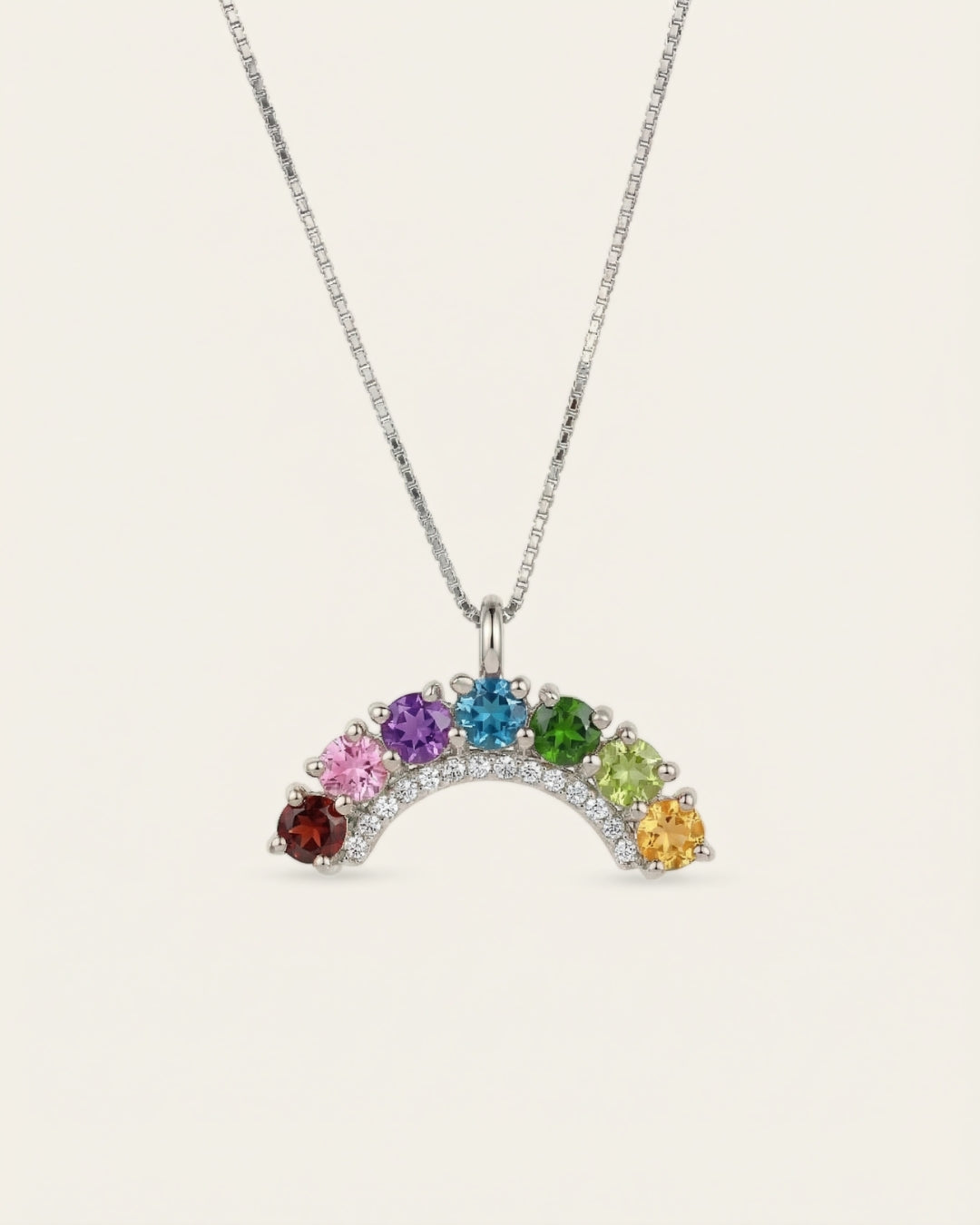 Symmetrical front view of a silver rainbow gemstone crescent arch pendant necklace on a clean minimal backdrop.
