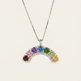 Symmetrical front view of a silver rainbow gemstone crescent arch pendant necklace on a clean minimal backdrop.
