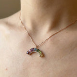 Close-up view of a rose gold multi-colored gemstone rainbow crescent necklace with a delicate crystal halo.