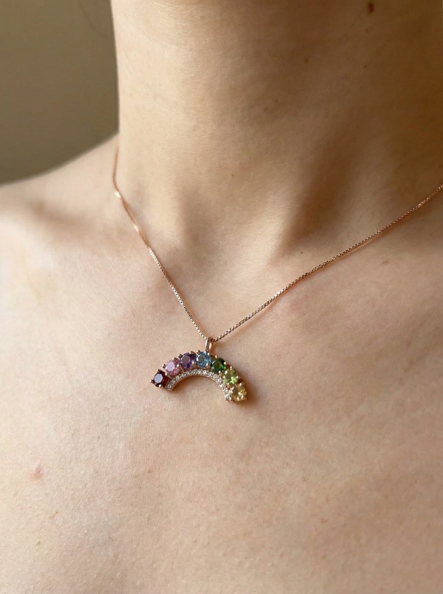 Close-up view of a rose gold multi-colored gemstone rainbow crescent necklace with a delicate crystal halo.
