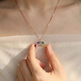 Model holding a curved natural gemstone rainbow arc pendant necklace to show detail and fit.