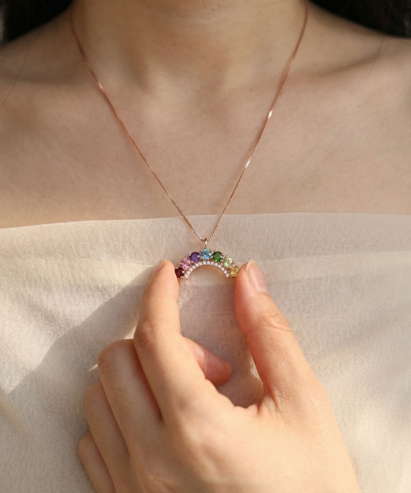 Model holding a curved natural gemstone rainbow arc pendant necklace to show detail and fit.