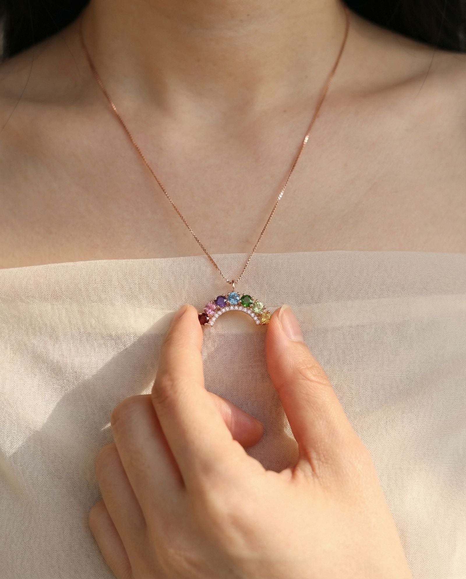 Model holding a curved natural gemstone rainbow arc pendant necklace to show detail and fit.