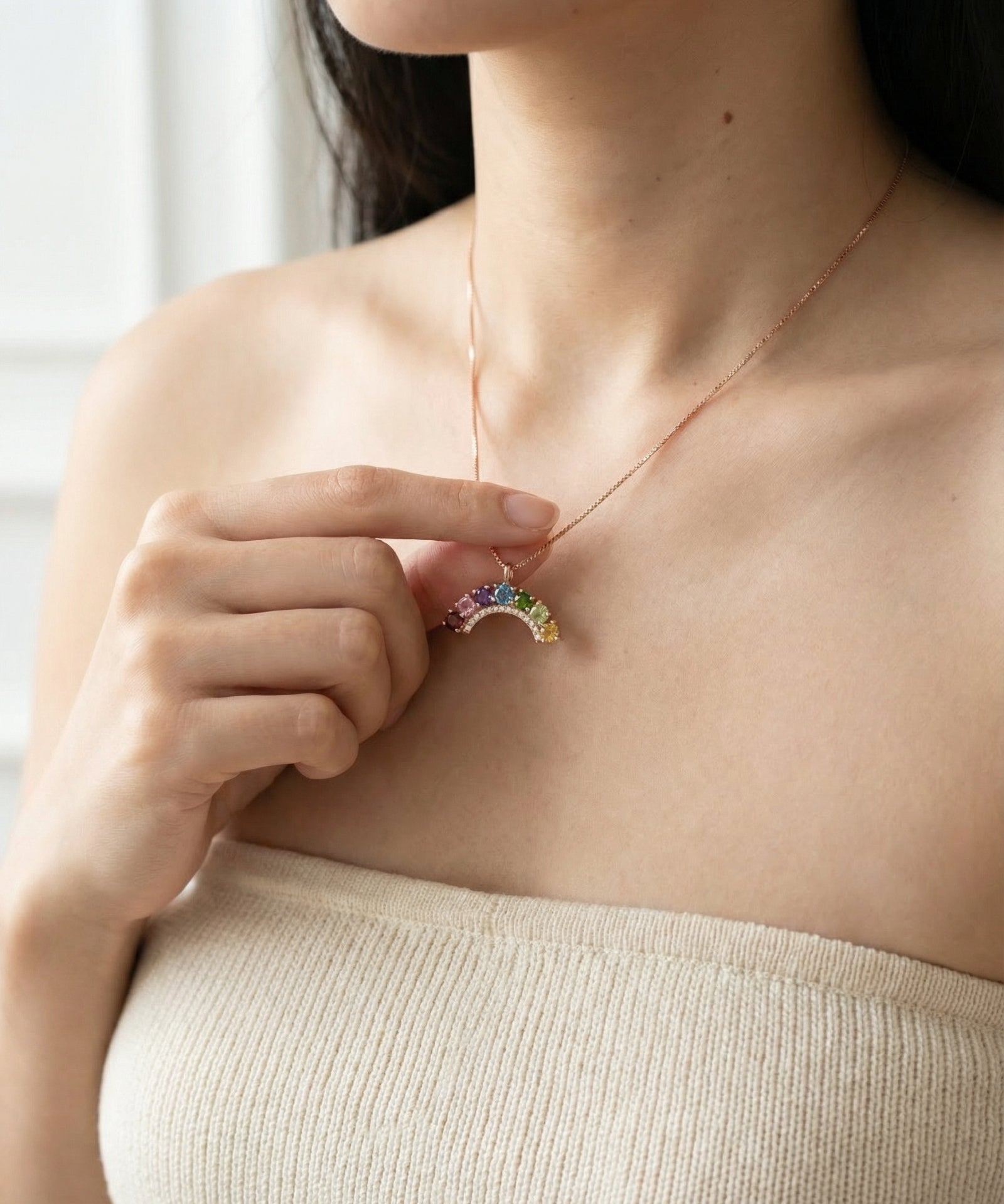 Model styling a dainty 18k rose gold vermeil rainbow arch gemstone necklace along the collarbone.