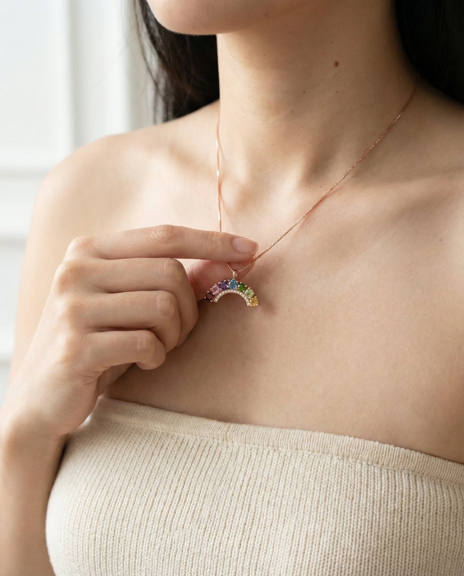 Model styling a dainty 18k rose gold vermeil rainbow arch gemstone necklace along the collarbone.