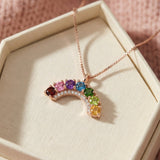 Rose gold rainbow arc necklace featuring garnet, topaz, diopside, and citrine resting in a textured beige jewelry gift box.
