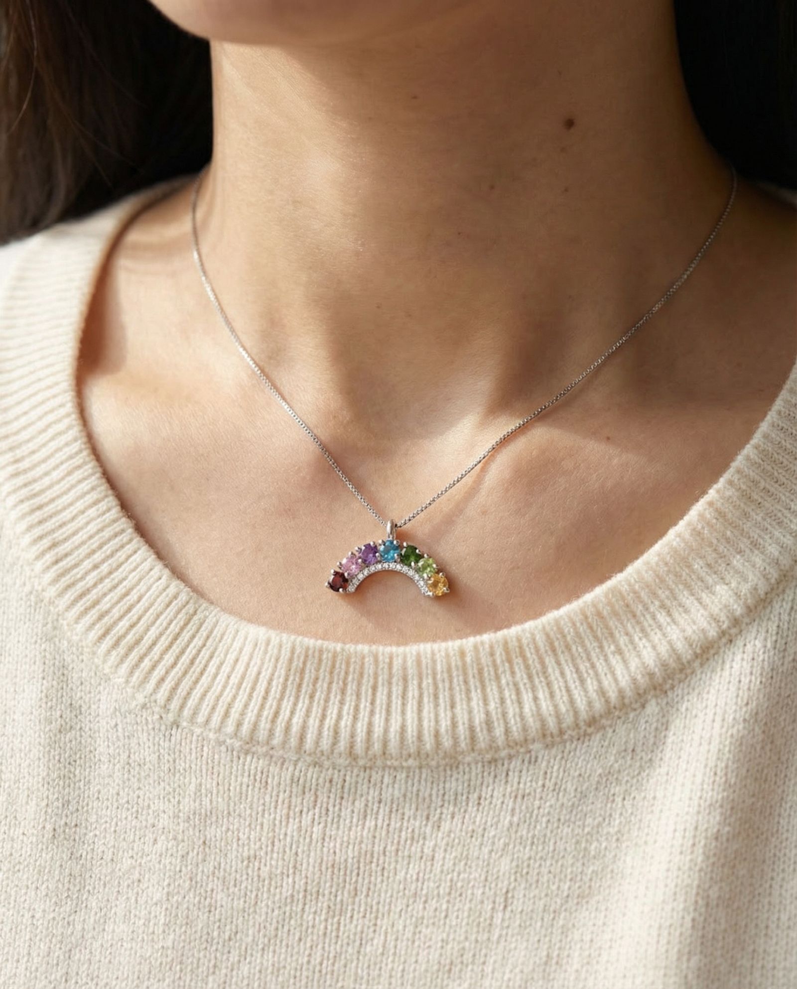 Model wearing a 925 sterling silver rainbow arc necklace with natural gradient gemstones against a cream knit sweater.