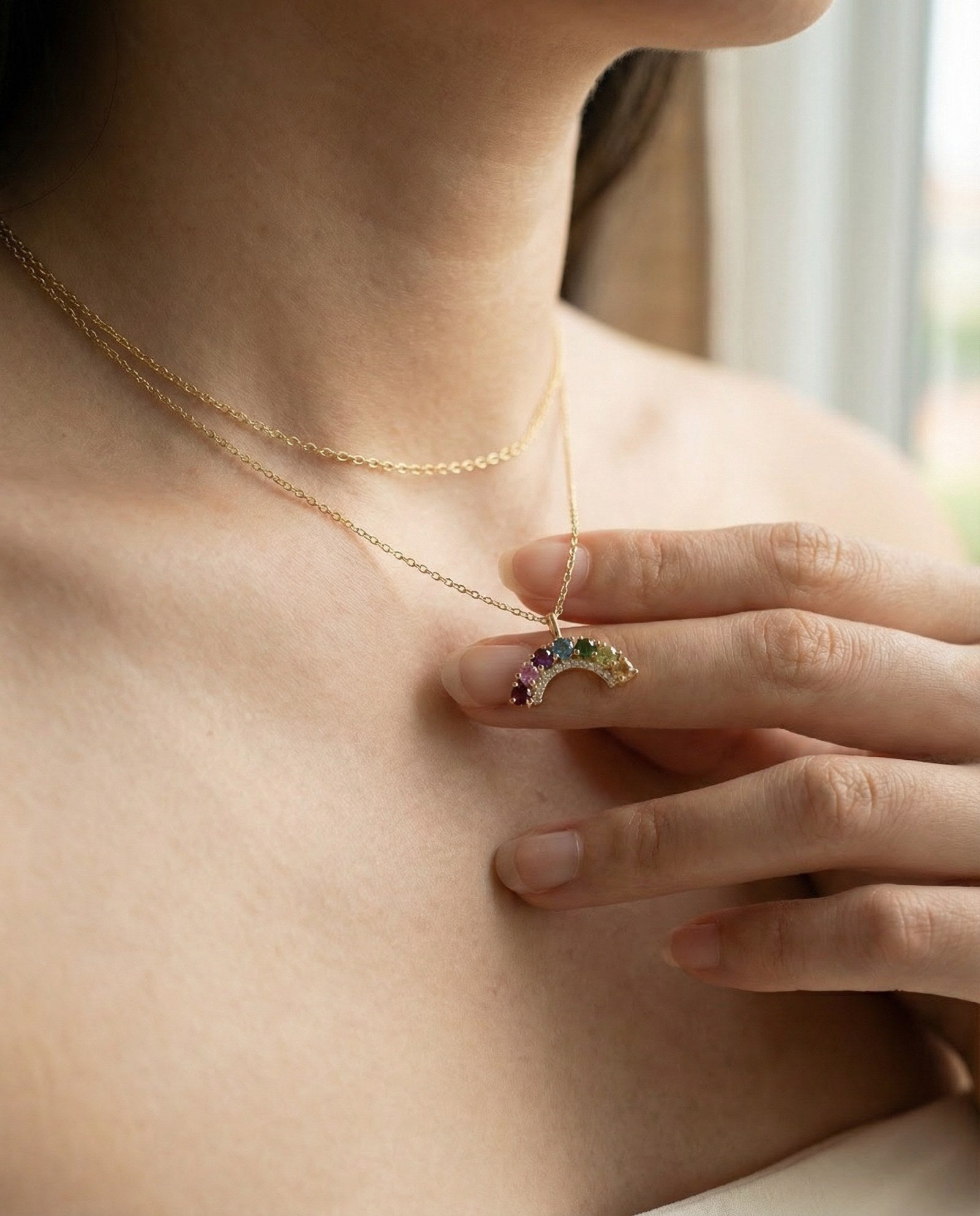Close-up of a model wearing a yellow gold multi-gemstone rainbow crescent pendant necklace, showcasing the scale.