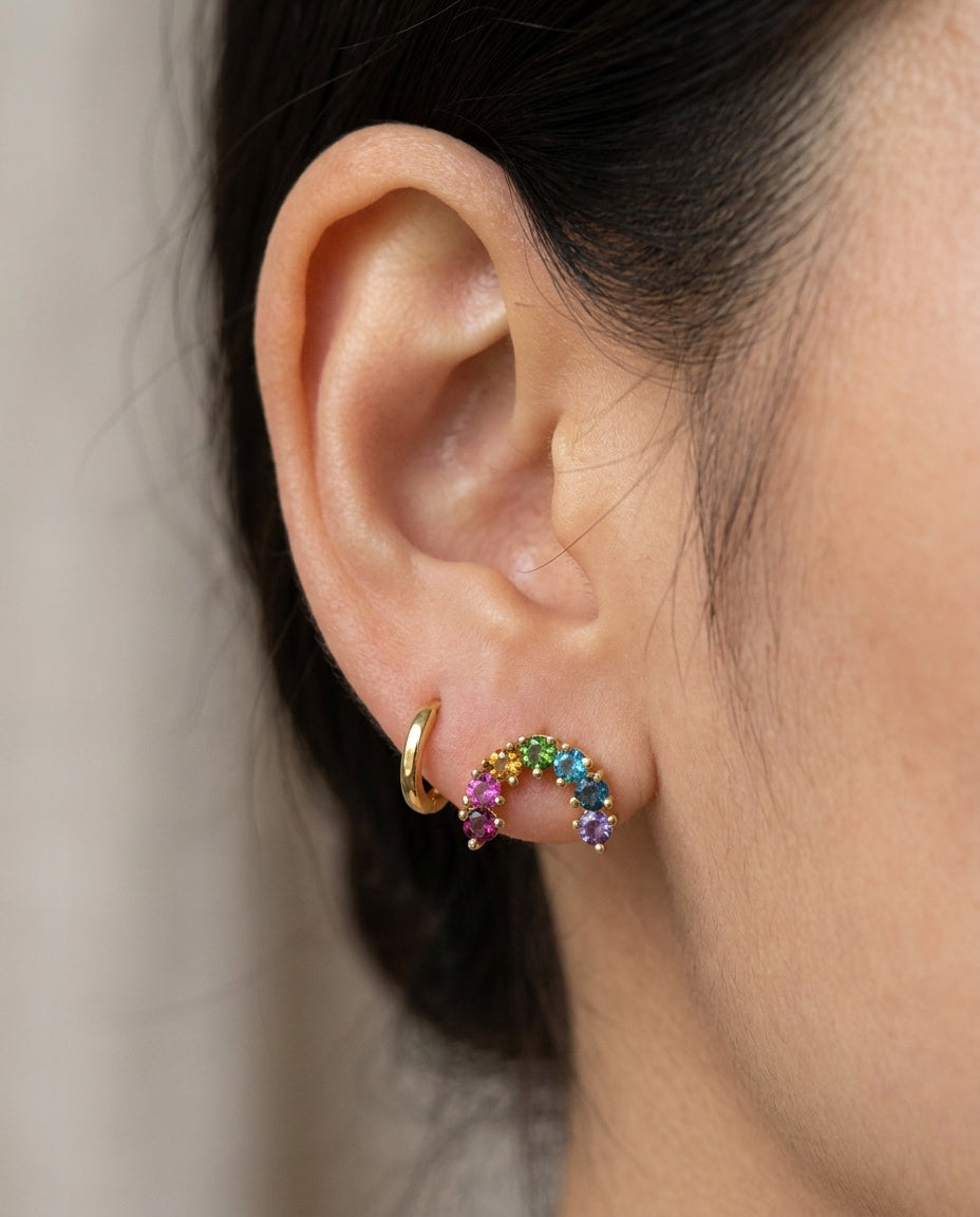 Side profile of a model styling a yellow gold rainbow multi-gemstone arc stud earring next to a small gold hoop.