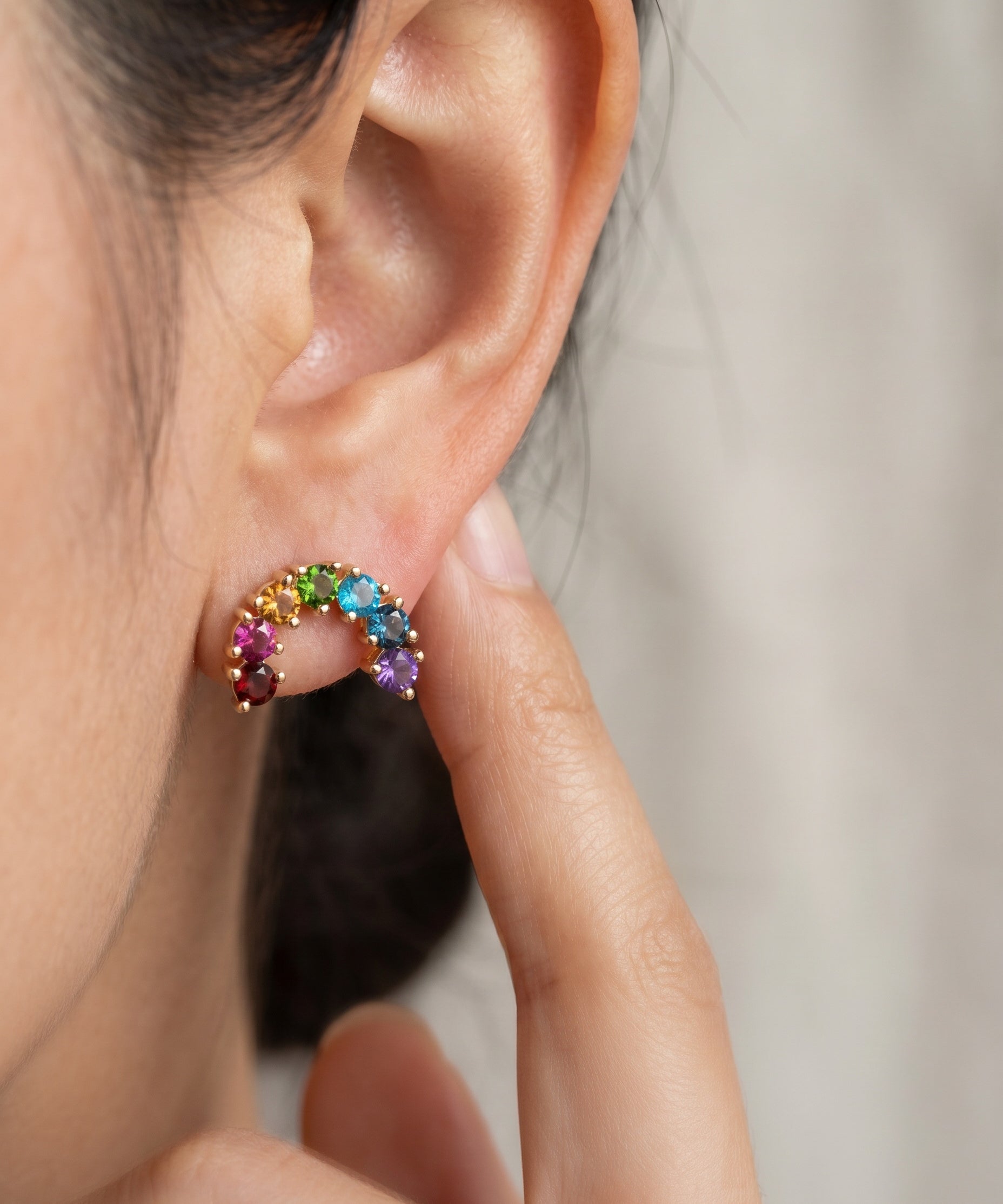 Model pointing to a yellow gold rainbow arc climber earring featuring a colorful natural gemstone gradient.