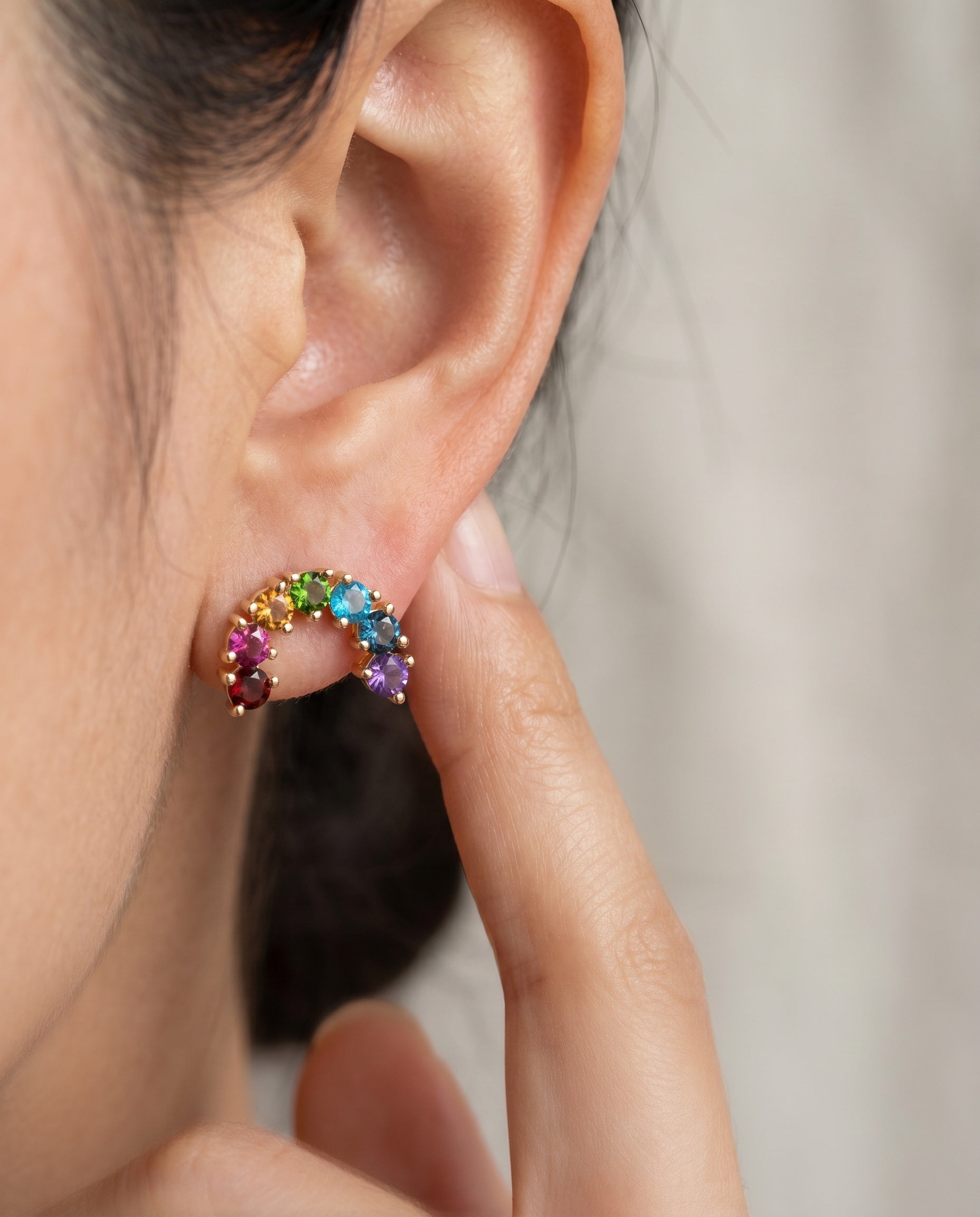 Model pointing to a yellow gold rainbow arc climber earring featuring a colorful natural gemstone gradient.
