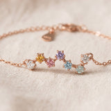 A macro close-up photograph of the rose gold Pastel Constellation Moissanite Bracelet resting on textured fabric, capturing the crisp prong details and the clear brilliance of the gradient pastel stones.