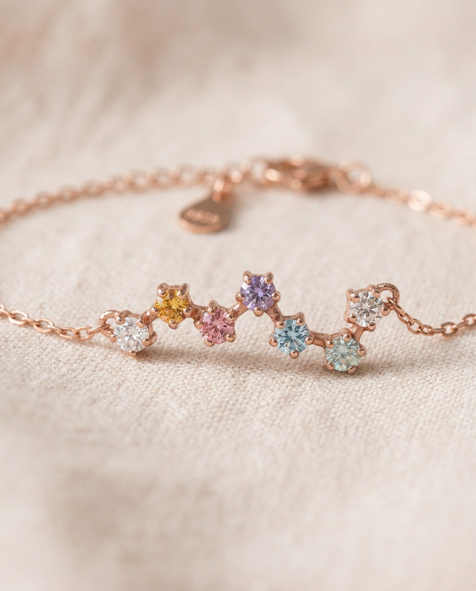 A macro close-up photograph of the rose gold Pastel Constellation Moissanite Bracelet resting on textured fabric, capturing the crisp prong details and the clear brilliance of the gradient pastel stones.
