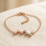 An angled tabletop lifestyle shot of the rose gold Pastel Constellation Moissanite Bracelet, showcasing the fine chain, clasp detail, and the wave-like constellation pattern of the multi-colored gems.