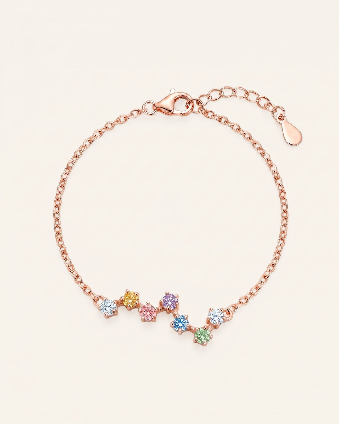 A top-down studio product photograph of the Pastel Constellation Moissanite Bracelet in rose gold, showcasing the delicate cable chain and the curved, zigzag star-cluster setting of multi-colored pastel gemstones.