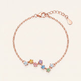 A top-down studio product photograph of the Pastel Constellation Moissanite Bracelet in rose gold, showcasing the delicate cable chain and the curved, zigzag star-cluster setting of multi-colored pastel gemstones.