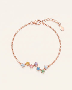 A top-down studio product photograph of the Pastel Constellation Moissanite Bracelet in rose gold, showcasing the delicate cable chain and the curved, zigzag star-cluster setting of multi-colored pastel gemstones.