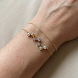 A close-up lifestyle photograph of the yellow gold Pastel Constellation Moissanite Bracelet being worn on a woman's wrist alongside a thin matching gold chain, demonstrating its delicate scale.