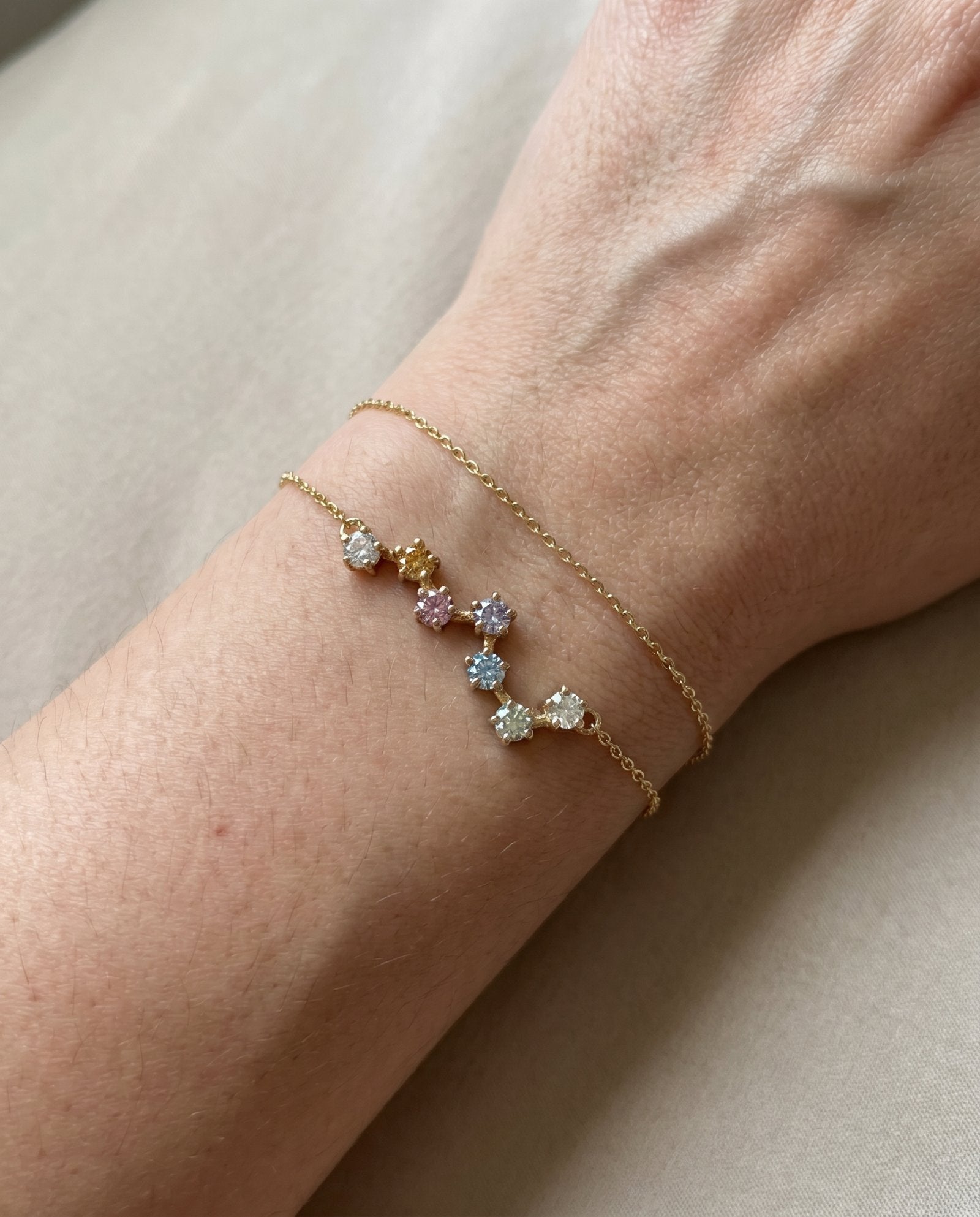 A close-up lifestyle photograph of the yellow gold Pastel Constellation Moissanite Bracelet being worn on a woman's wrist alongside a thin matching gold chain, demonstrating its delicate scale.