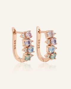 Close-up of the Pastel Moissanite Cluster Huggies in rose gold, resting on a warm linen background