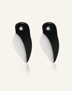 Close-up of the Penguin Parade Earrings in black gold, resting on a warm linen background