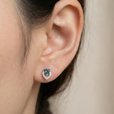 Model wearing the Petite Blue Tourmaline Heart Studs in silver, showing the delicate size and "double heart" design on the ear.