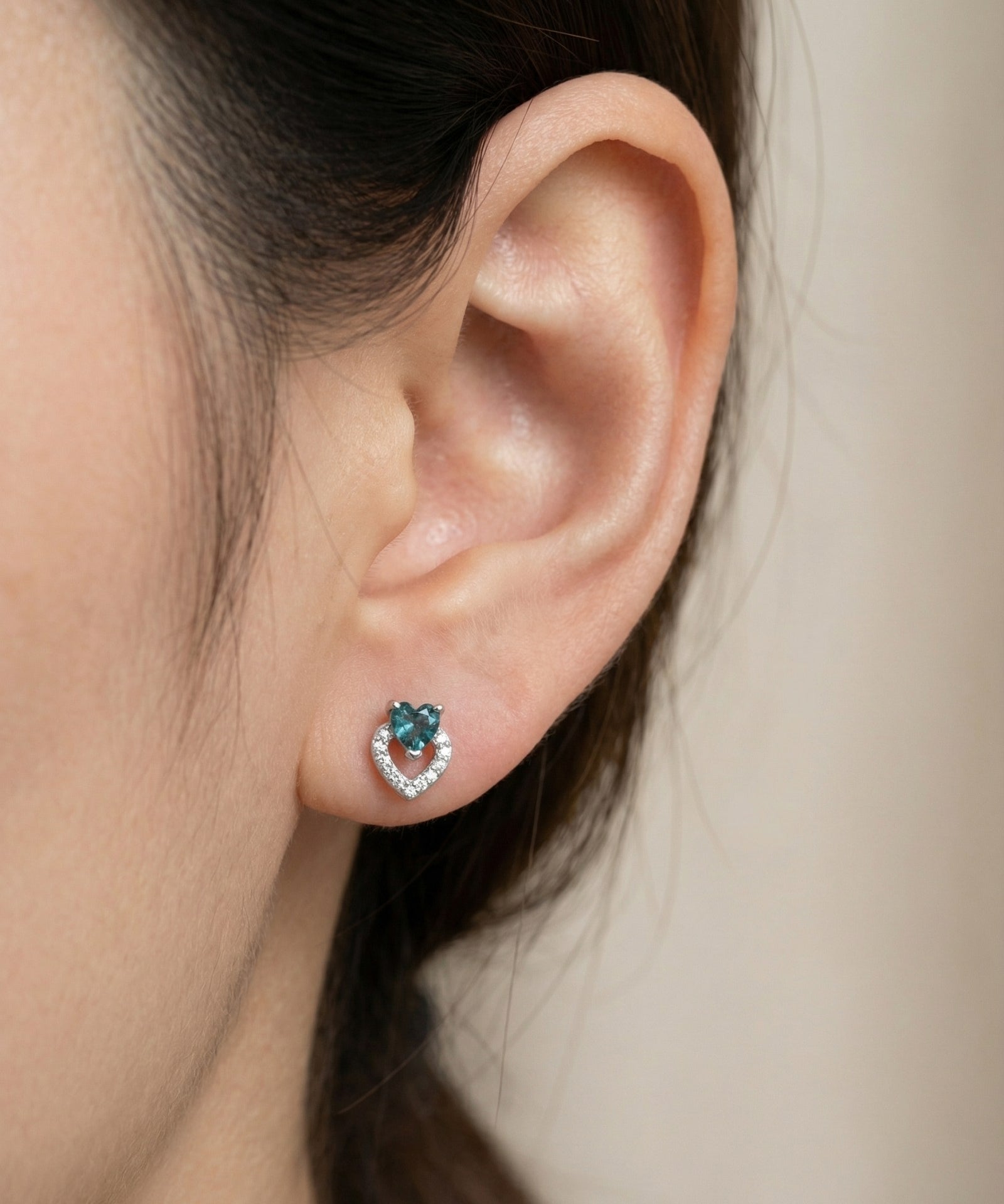 Model wearing the Petite Blue Tourmaline Heart Studs in silver, showing the delicate size and "double heart" design on the ear.