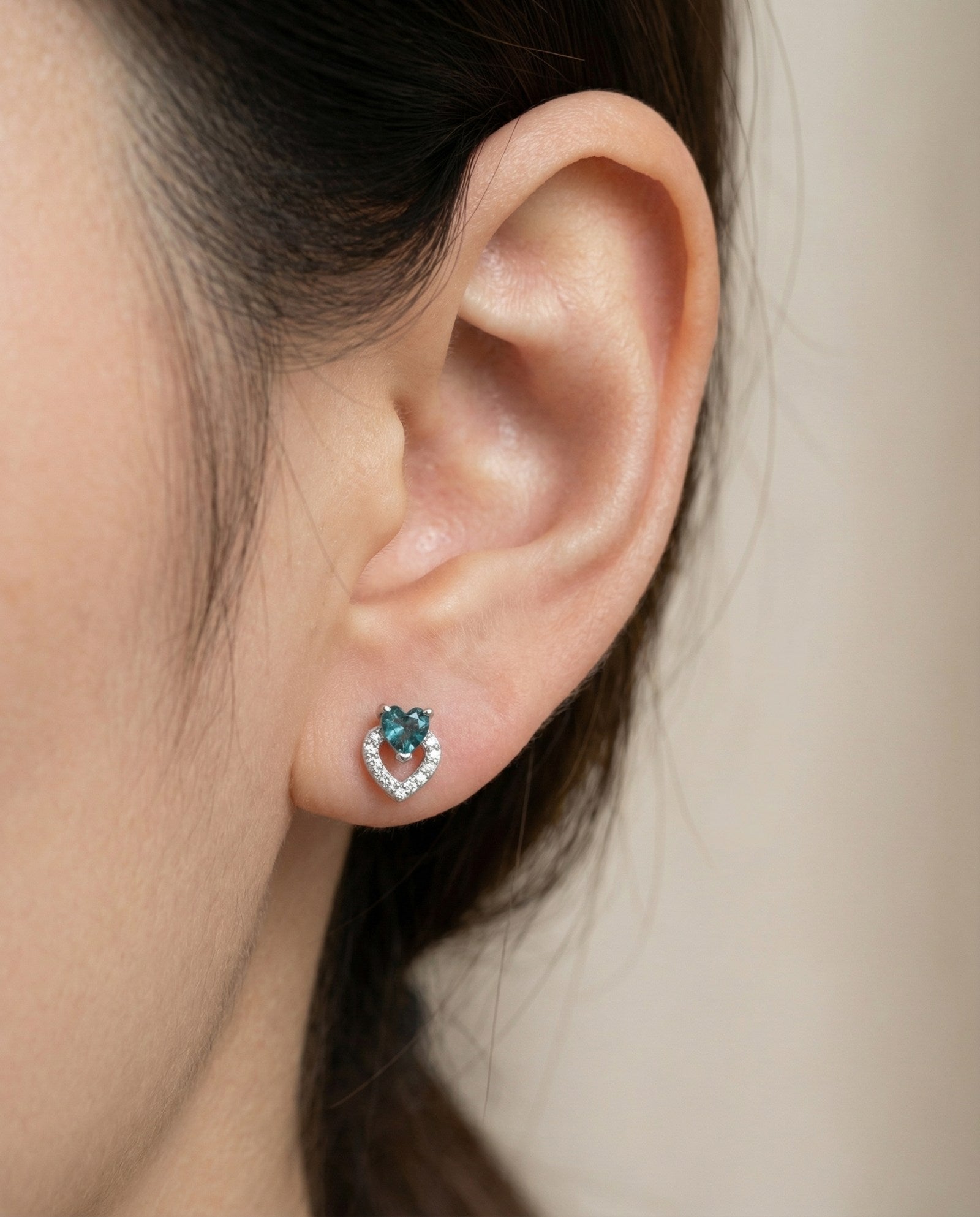 Model wearing the Petite Blue Tourmaline Heart Studs in silver, showing the delicate size and "double heart" design on the ear.