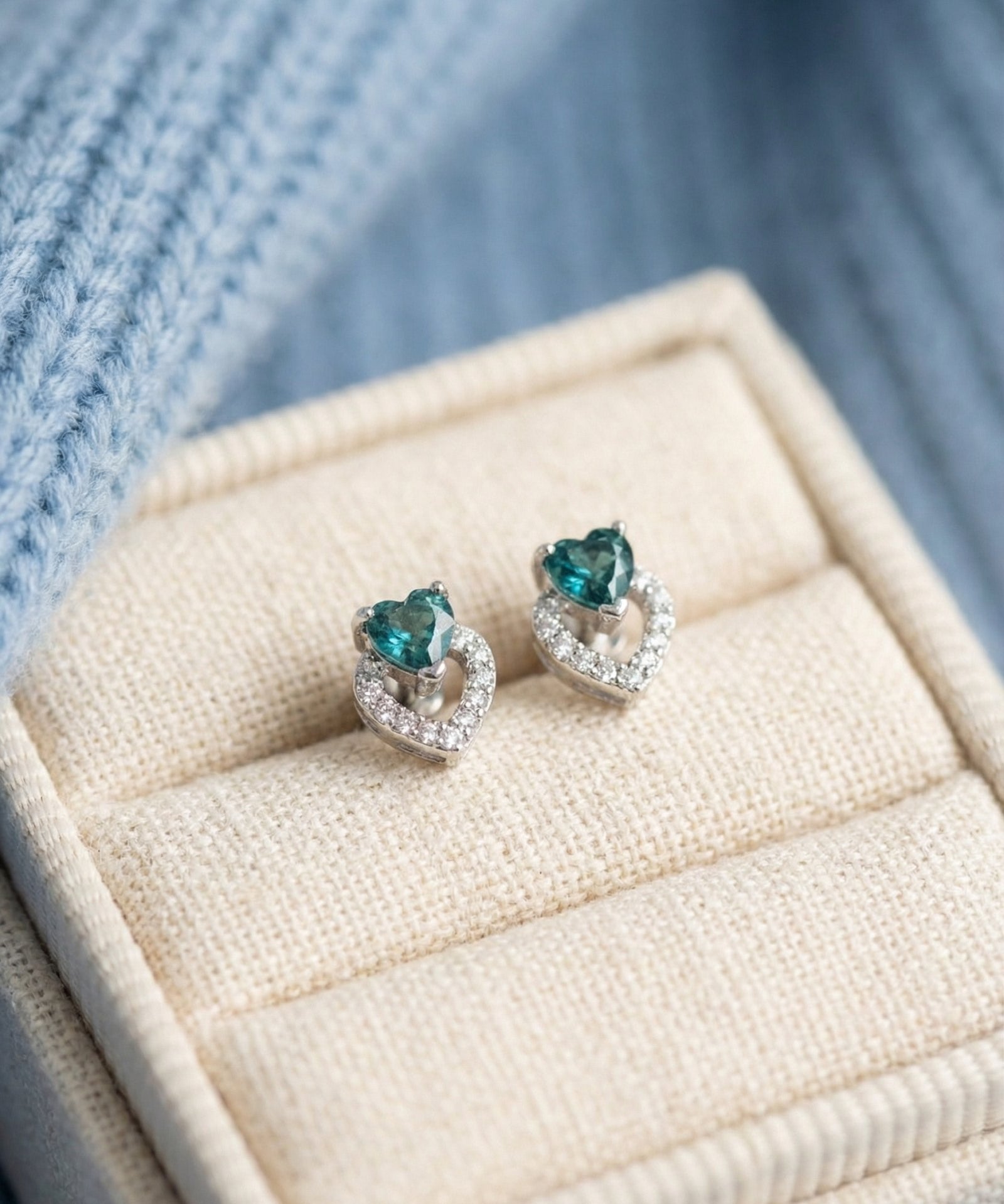 Petite double heart stud earrings featuring teal-blue tourmaline gemstones in a high-quality linen jewelry box.