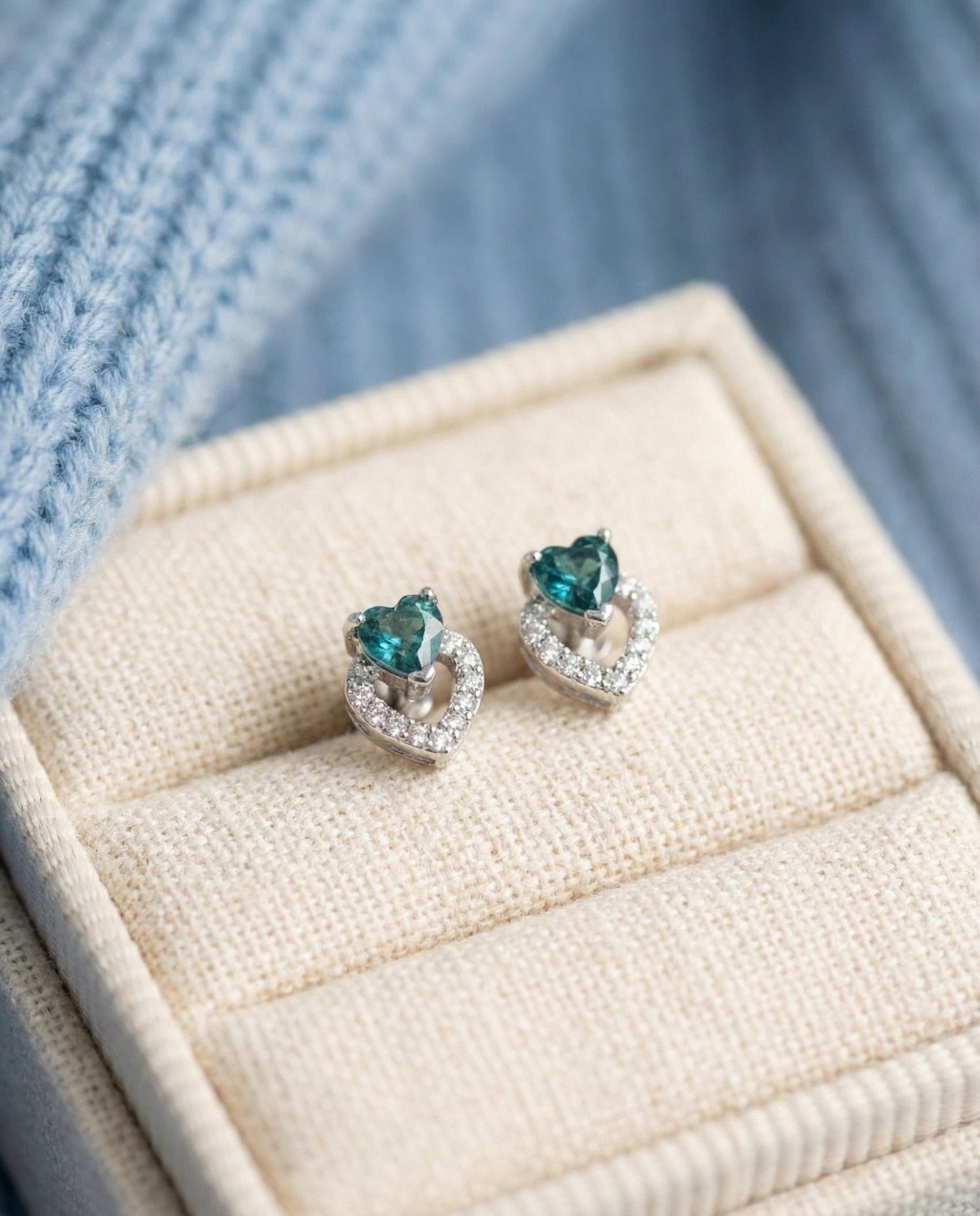 Petite double heart stud earrings featuring teal-blue tourmaline gemstones in a high-quality linen jewelry box.