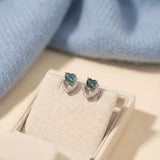 Close-up of Petite Blue Tourmaline Heart Studs in a cream jewelry box with a soft blue knit background.