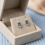 Angled view of heart-cut blue tourmaline earrings with a shimmering pavé heart frame in a luxury gift box.