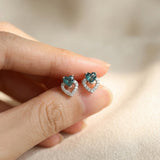 Hand-held view of Petite Blue Tourmaline Heart Studs in silver to show scale and the vibrant blue-green gemstone color.