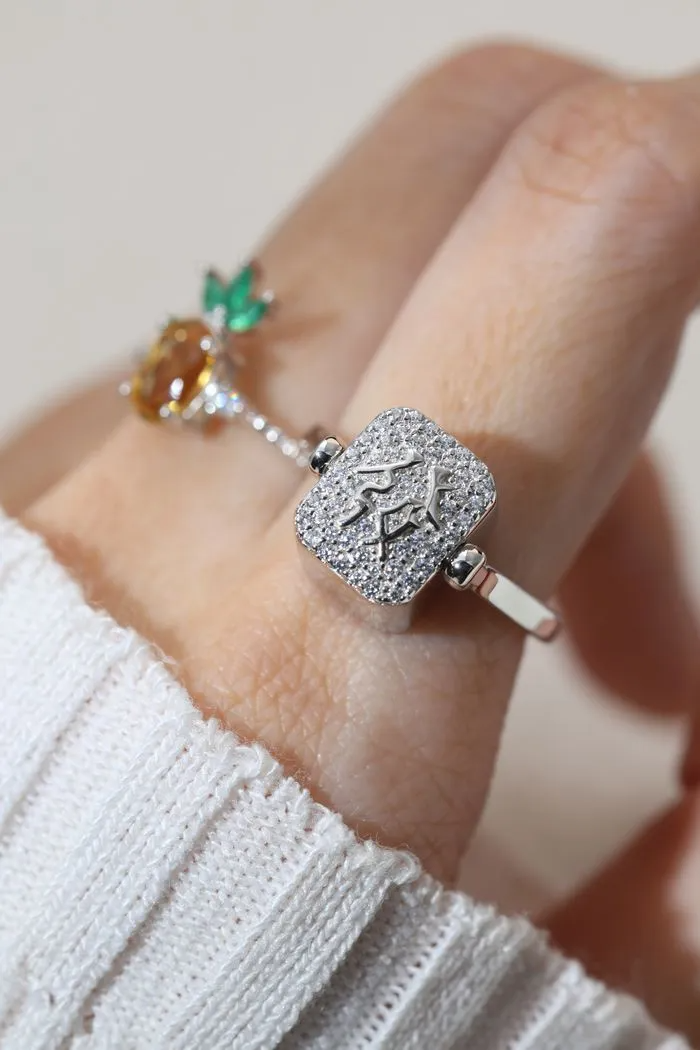 A model wearing a silver ring featuring a reversible rectangular citrine gemstone adorned with intricate carvings and surrounded by cubic zirconias.
