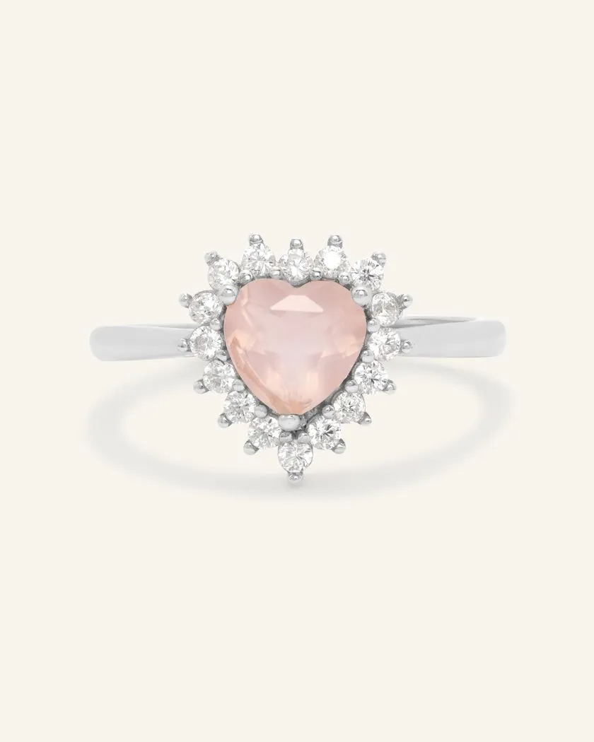 A silver ring featuring a heart-shaped rose quartz center stone, surrounded by a halo of sparkling cubic zirconias.