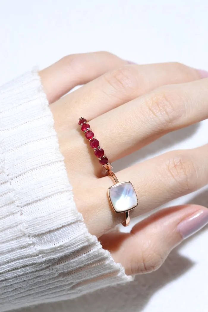 A model wearing the ruby half eternity band. The ring features a series of vibrant, deep red round-cut rubies set in a rose gold band, arranged in a continuous line around half of the band, showcasing a timeless and elegant design.