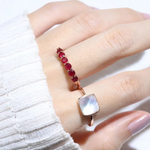 A model wearing the ruby half eternity band. The ring features a series of vibrant, deep red round-cut rubies set in a rose gold band, arranged in a continuous line around half of the band, showcasing a timeless and elegant design.