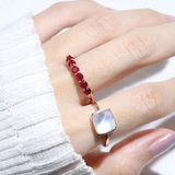 A model wearing the ruby half eternity band. The ring features a series of vibrant, deep red round-cut rubies set in a rose gold band, arranged in a continuous line around half of the band, showcasing a timeless and elegant design.