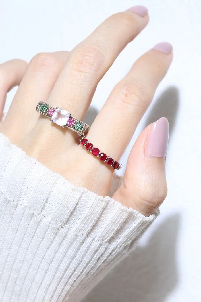 A model wearing the ruby half eternity band. The ring features a series of vibrant, deep red round-cut rubies set in a silver band, arranged in a continuous line around half of the band, showcasing a timeless and elegant design.