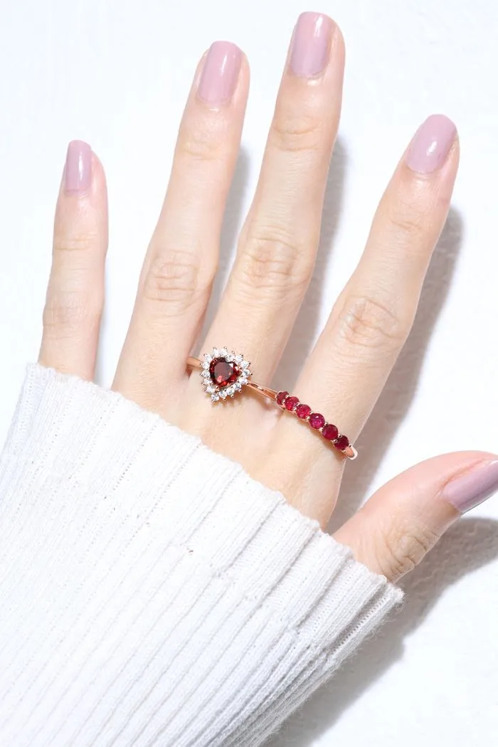 A model wearing the ruby half eternity band. The ring features a series of vibrant, deep red round-cut rubies set in a rose gold band, arranged in a continuous line around half of the band, showcasing a timeless and elegant design.
