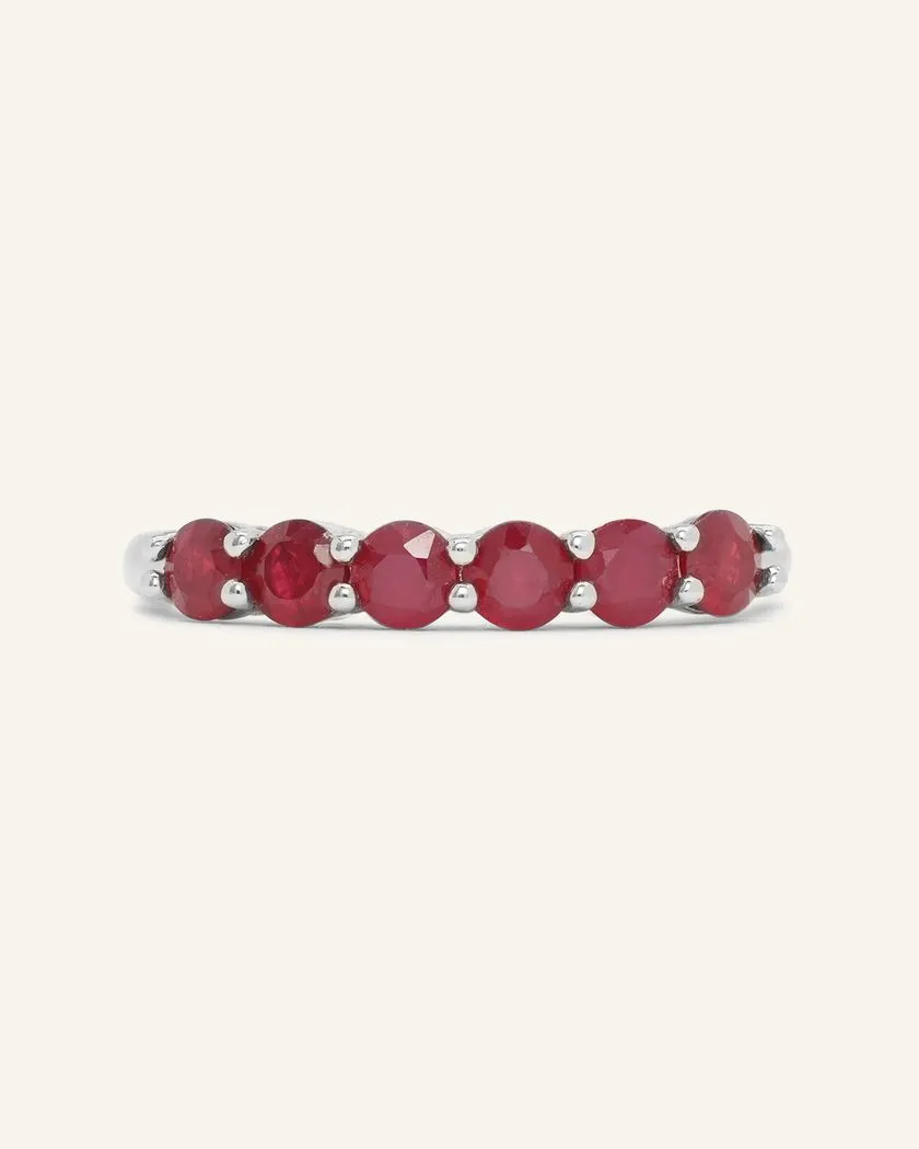 A close-up image of a ruby half eternity band. The ring features a series of vibrant, deep red round-cut rubies set in a silver band, arranged in a continuous line around half of the band, showcasing a timeless and elegant design.