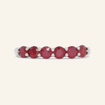 A close-up image of a ruby half eternity band. The ring features a series of vibrant, deep red round-cut rubies set in a silver band, arranged in a continuous line around half of the band, showcasing a timeless and elegant design.