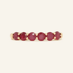 A close-up image of a ruby half eternity band. The ring features a series of vibrant, deep red round-cut rubies set in a yellow gold band, arranged in a continuous line around half of the band, showcasing a timeless and elegant design.