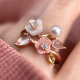 A model wearing the rose gold Sakura Symphony Ring adorned with peridot, freshwater pearl, rose quartz, hand-carved shell flowers, and sparkling moissanite accents, capturing the essence of spring blossoms.