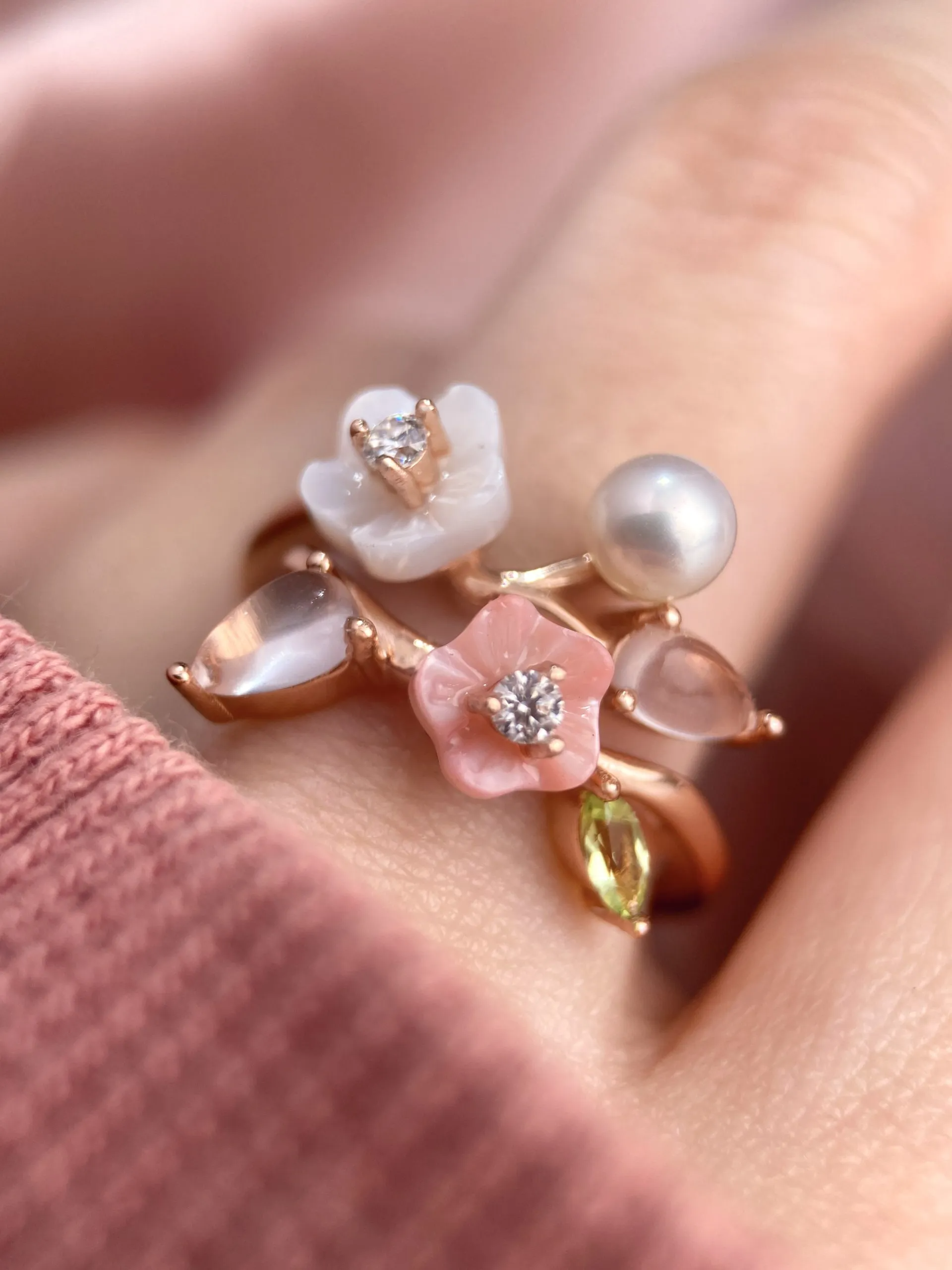 A model wearing the rose gold Sakura Symphony Ring adorned with peridot, freshwater pearl, rose quartz, hand-carved shell flowers, and sparkling moissanite accents, capturing the essence of spring blossoms.